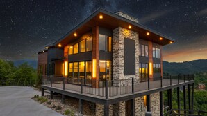 Une maison moderne à deux étages, dotée d’un balcon, de grandes fenêtres et d’une façade en pierre.