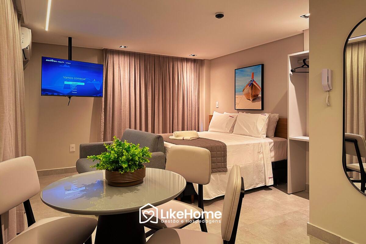 Ett modernt hotellrum med en säng, ett skrivbord, en tv och en krukväxt.