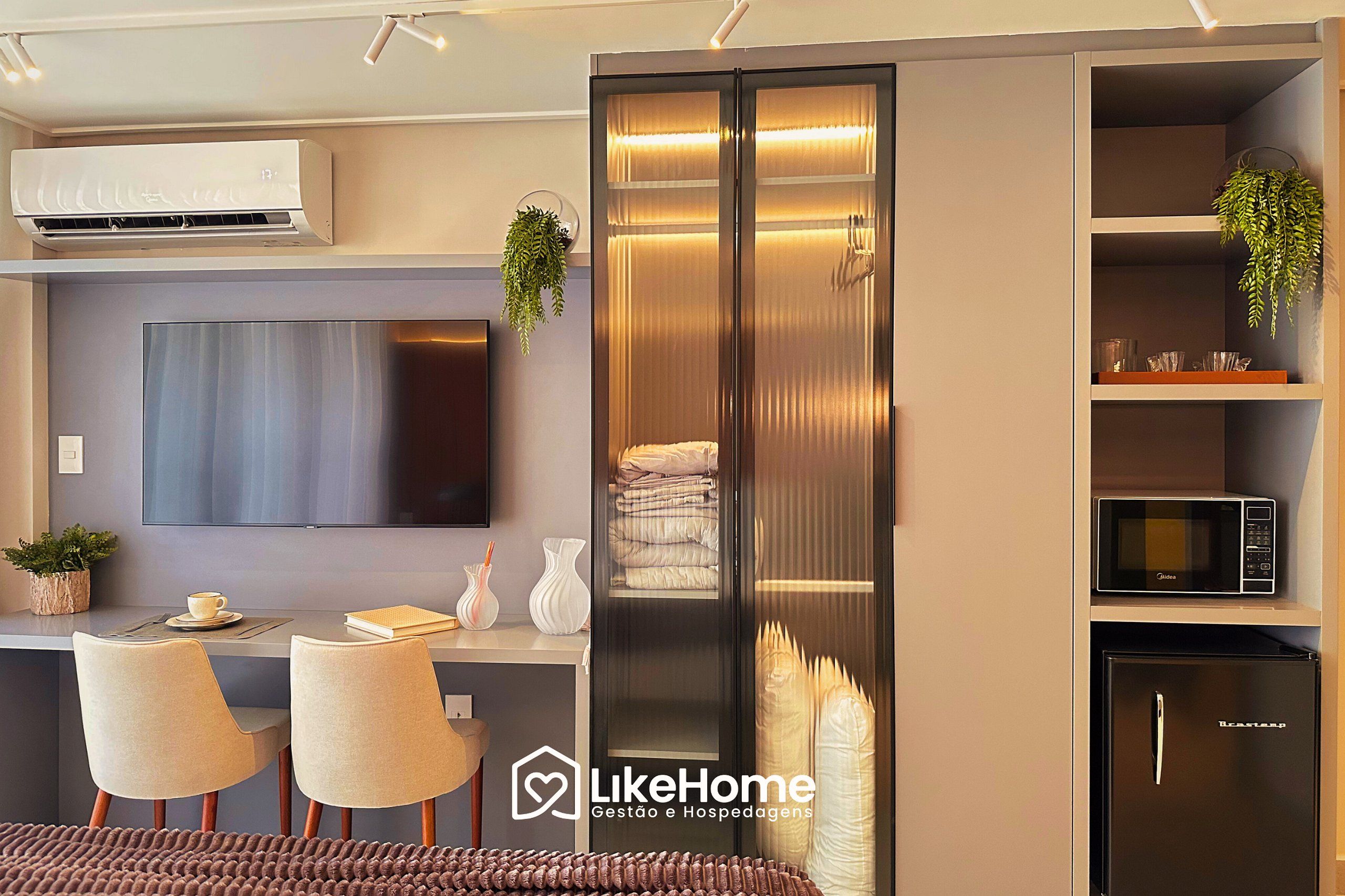 Una sala moderna con un televisor de pantalla plana, aire acondicionado integrado, comedor con sillas, un sofá y una cocina con microondas y refrigerador.