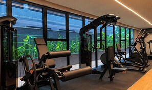 Een sportschool met diverse fitnessapparatuur, grote ramen en uitzicht op groen.