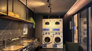 A modern bathroom with a marble sink, two stacked washing machines, and a small plant.