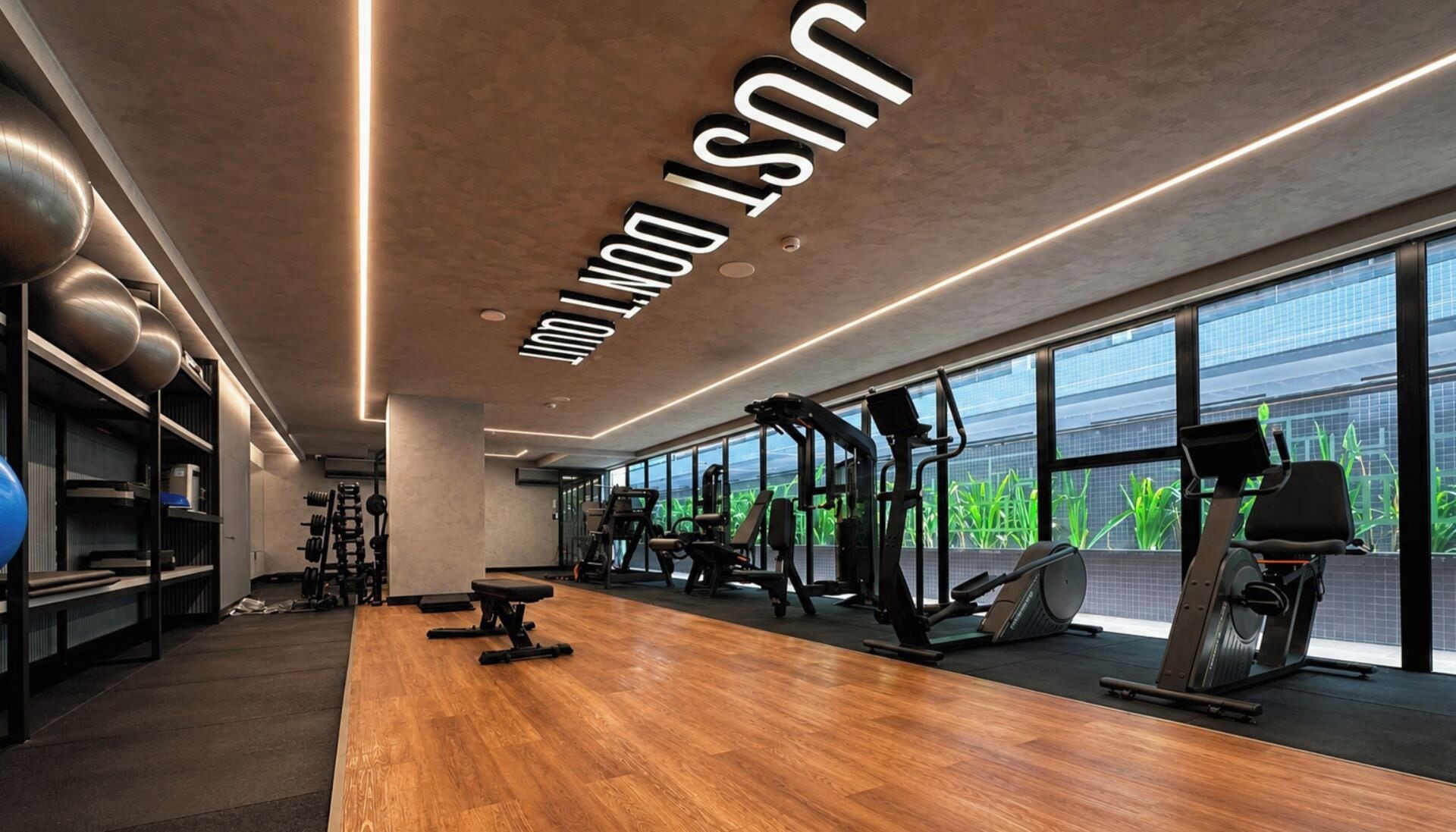 A modern gym with exercise equipment, large windows, and a wooden floor.