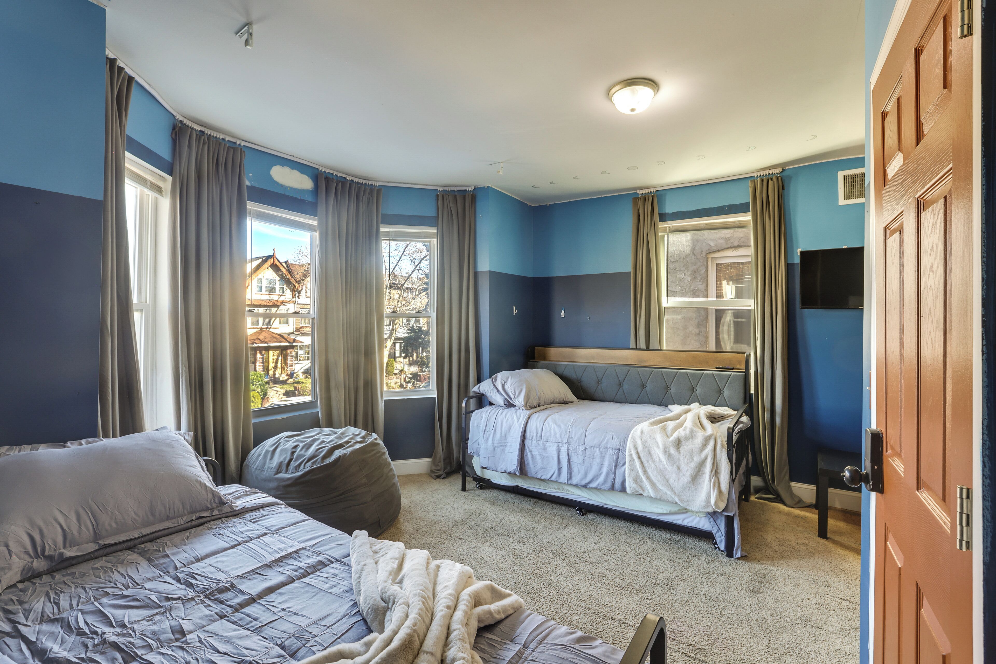 A bedroom with two beds, a large window, and a view of a house outside.
