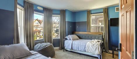 A bedroom with two beds, a large window, and a view of a house outside.