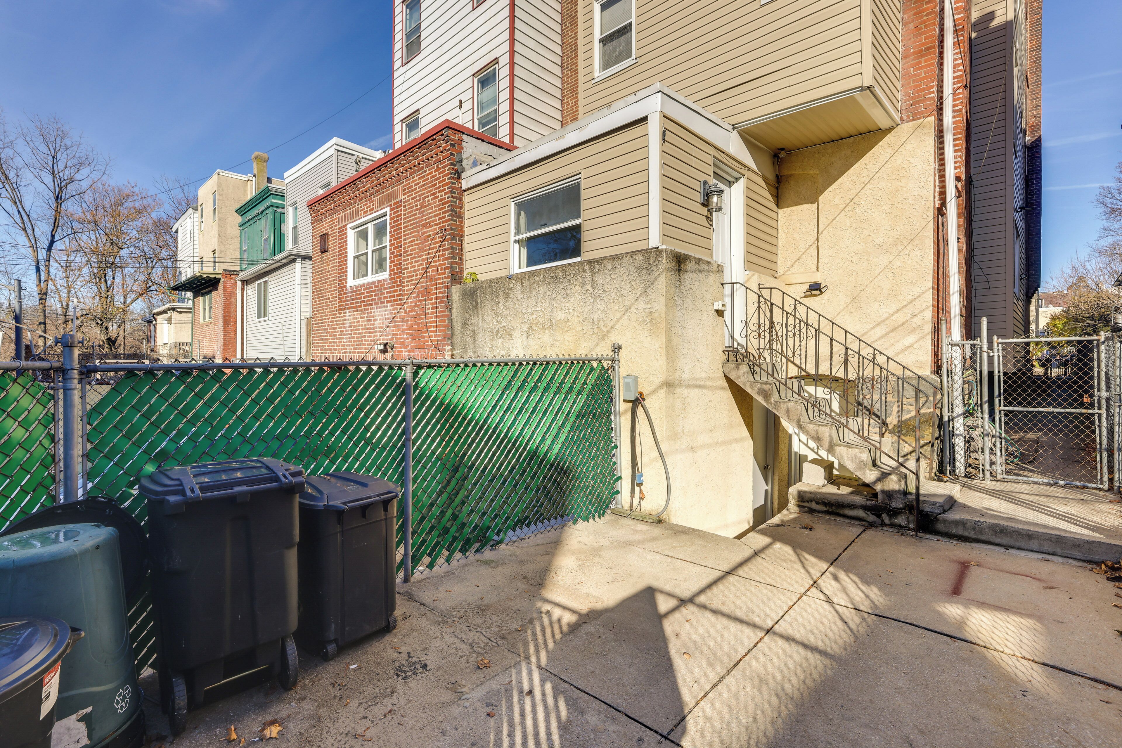 A multi-story residential building with a green fence, a concrete staircase, and black trash bins.