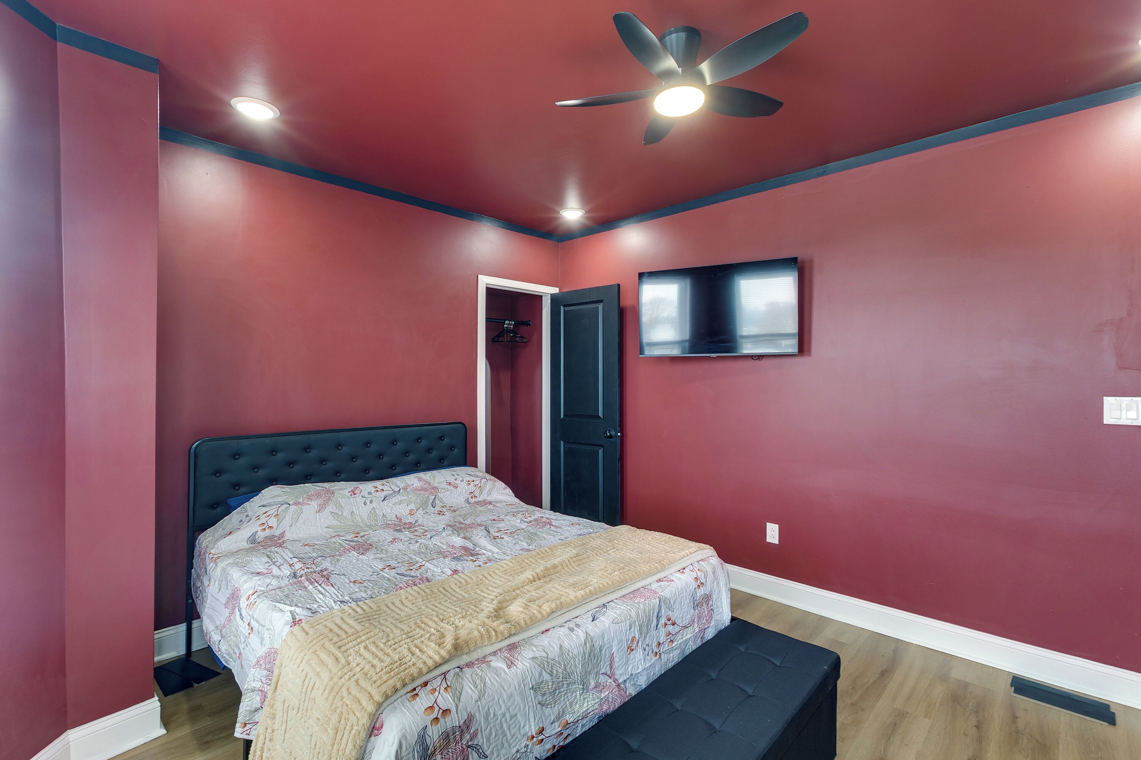 A bedroom with a bed, a ceiling fan, a TV, and a door.