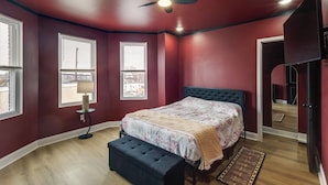 Une chambre à coucher comprenant un lit, un banc, un ventilateur de plafond et deux fenêtres équipées de stores.