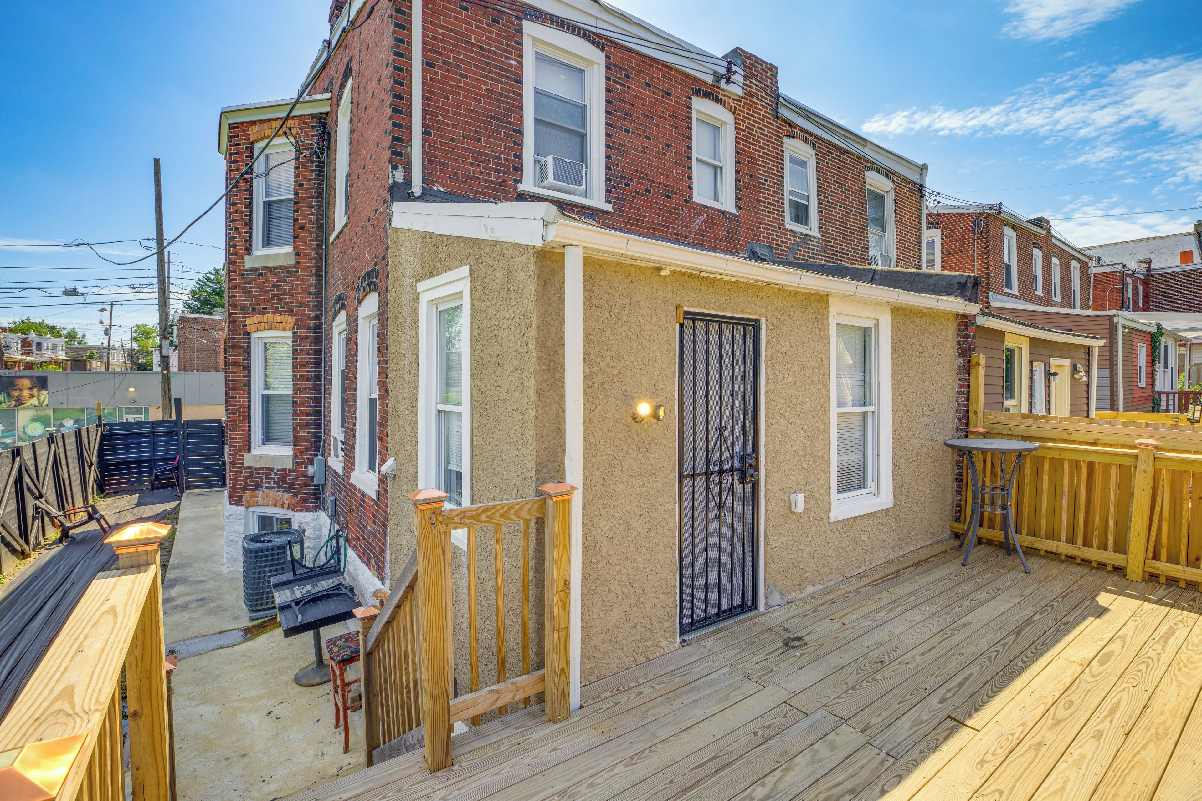 A two-story brick house with a wooden deck, a black door, and a small outdoor seating area.