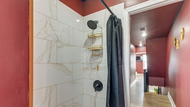 Une douche avec une étagère dorée, des carreaux de marbre et un rideau de douche foncé.