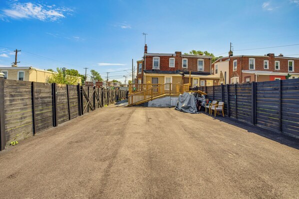 A residential driveway leading to a house with a wooden fence, a metal gate, and a covered area with chairs. - Colorful & Convenient Darby Apt, 7 Mi to Stadiums! (Darby)