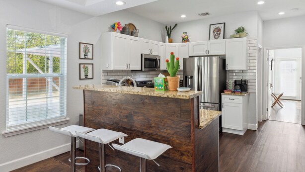A modern kitchen with white cabinets, stainless steel appliances, and a wooden island with bar stools. - Walk to Alamodome! Stylish Home w/ Private Parking (San Antonio)