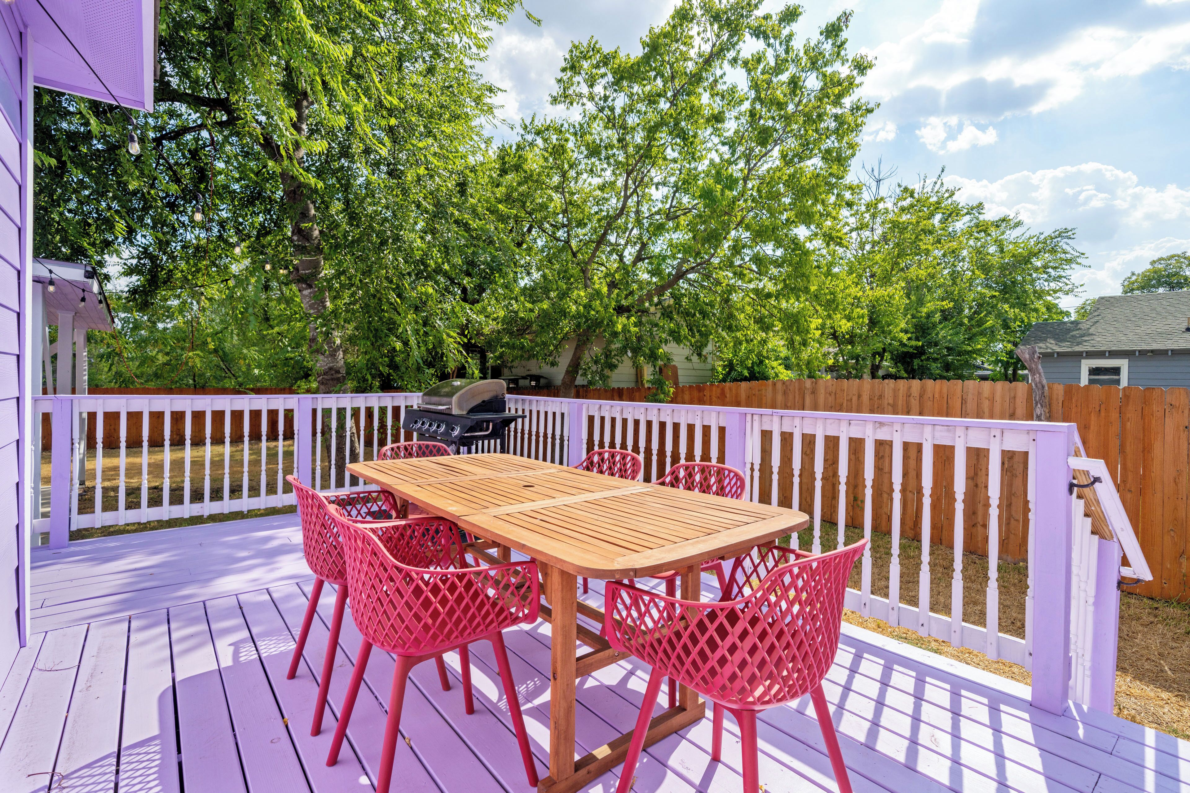 Een houten terras met een witte balustrade, omgeven door een paars huis en een houten schutting.