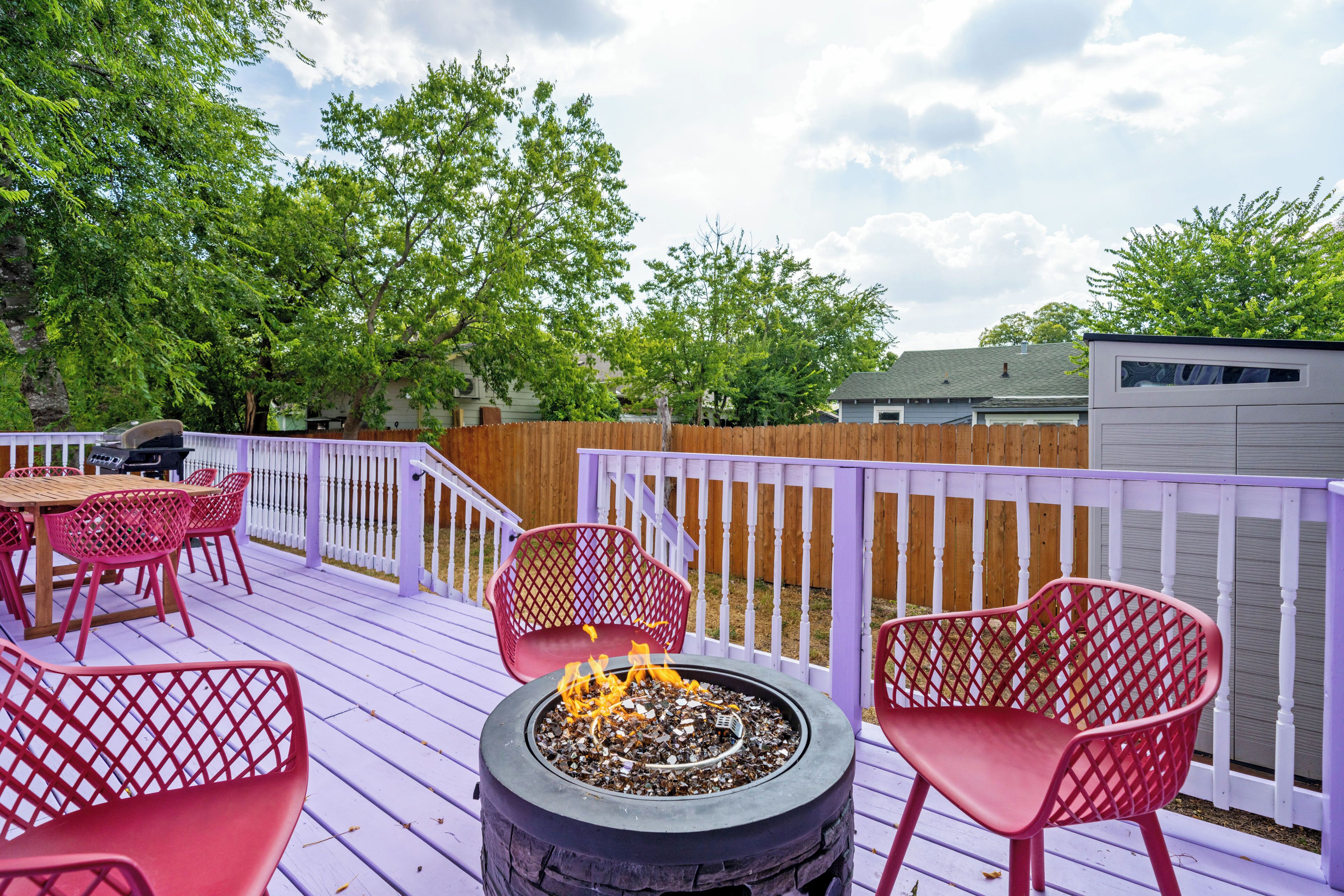 A deck with a fire pit, red chairs, and a table.