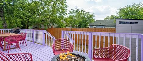 A deck with a fire pit, red chairs, and a table.
