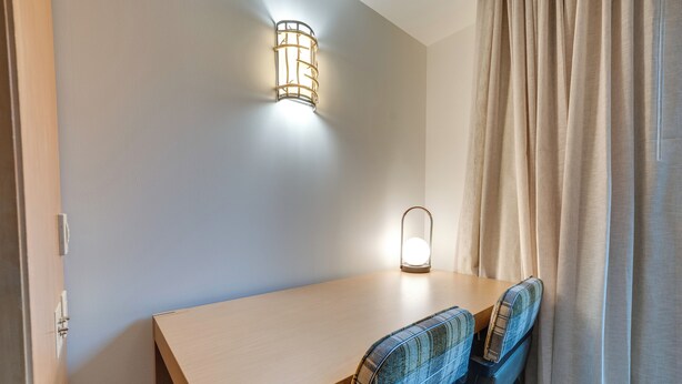 A small, neatly arranged room with a wooden desk, two plaid chairs, a wall-mounted light fixture, and a curtain on the right. - Beautiful Studio in Suncadia Resort (Cle Elum)