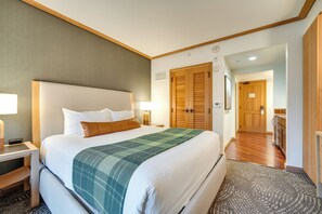 A hotel room with a large bed, a bedside table with a lamp, a wooden door, and a hallway leading to a bathroom. - Beautiful Studio in Suncadia Resort (Cle Elum)