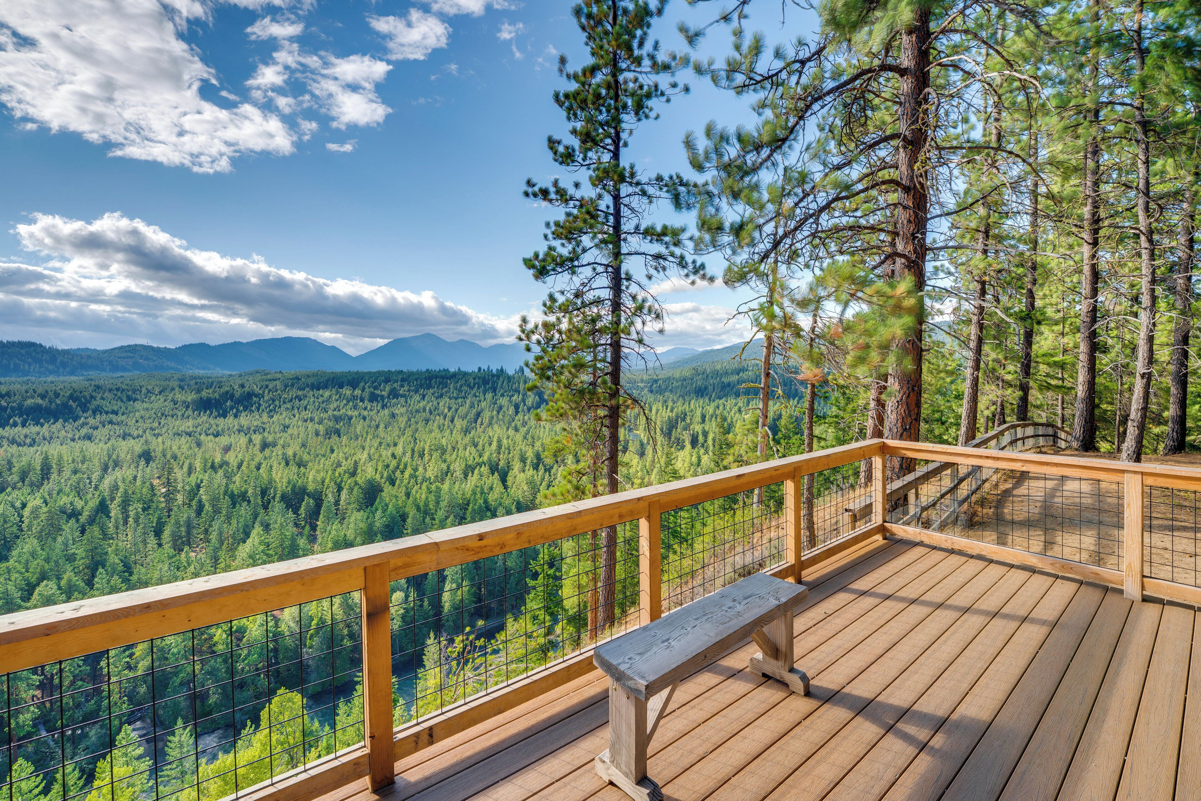 A wooden deck with a bench overlooking a forested valley and mountains.