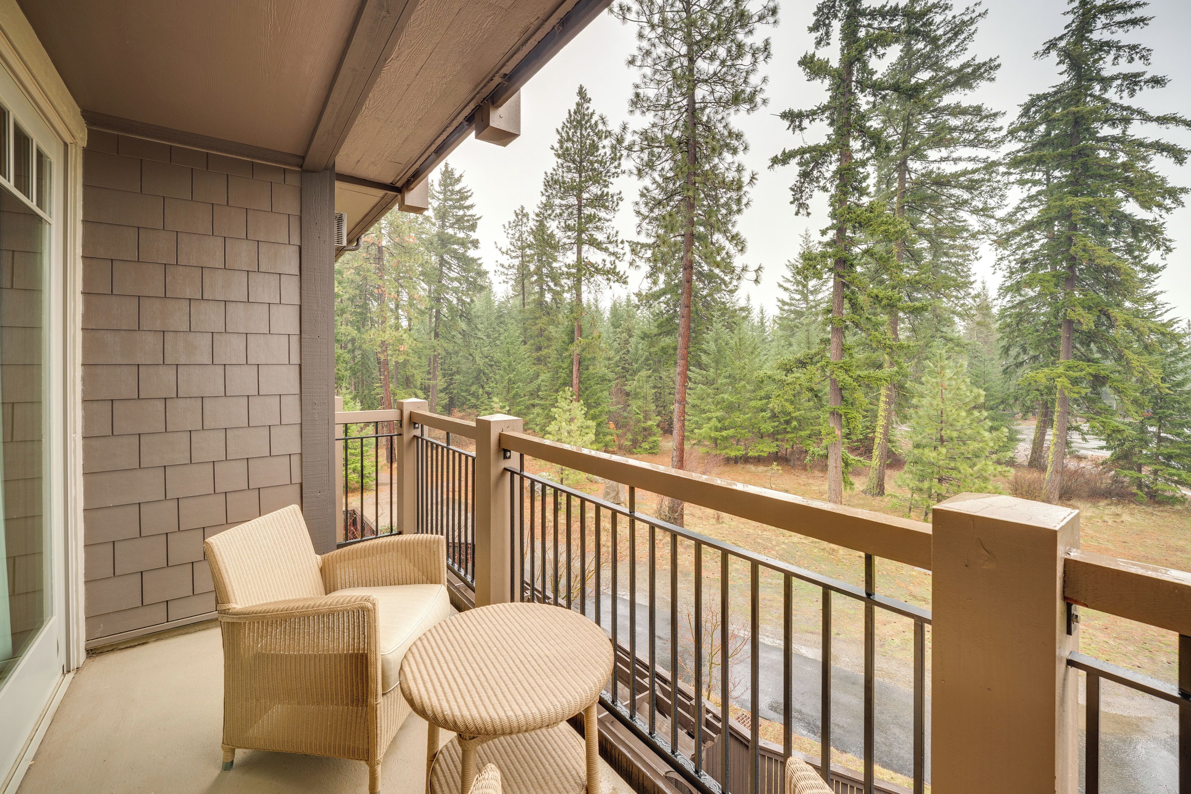 A balcony with wicker furniture and a view of tall trees.