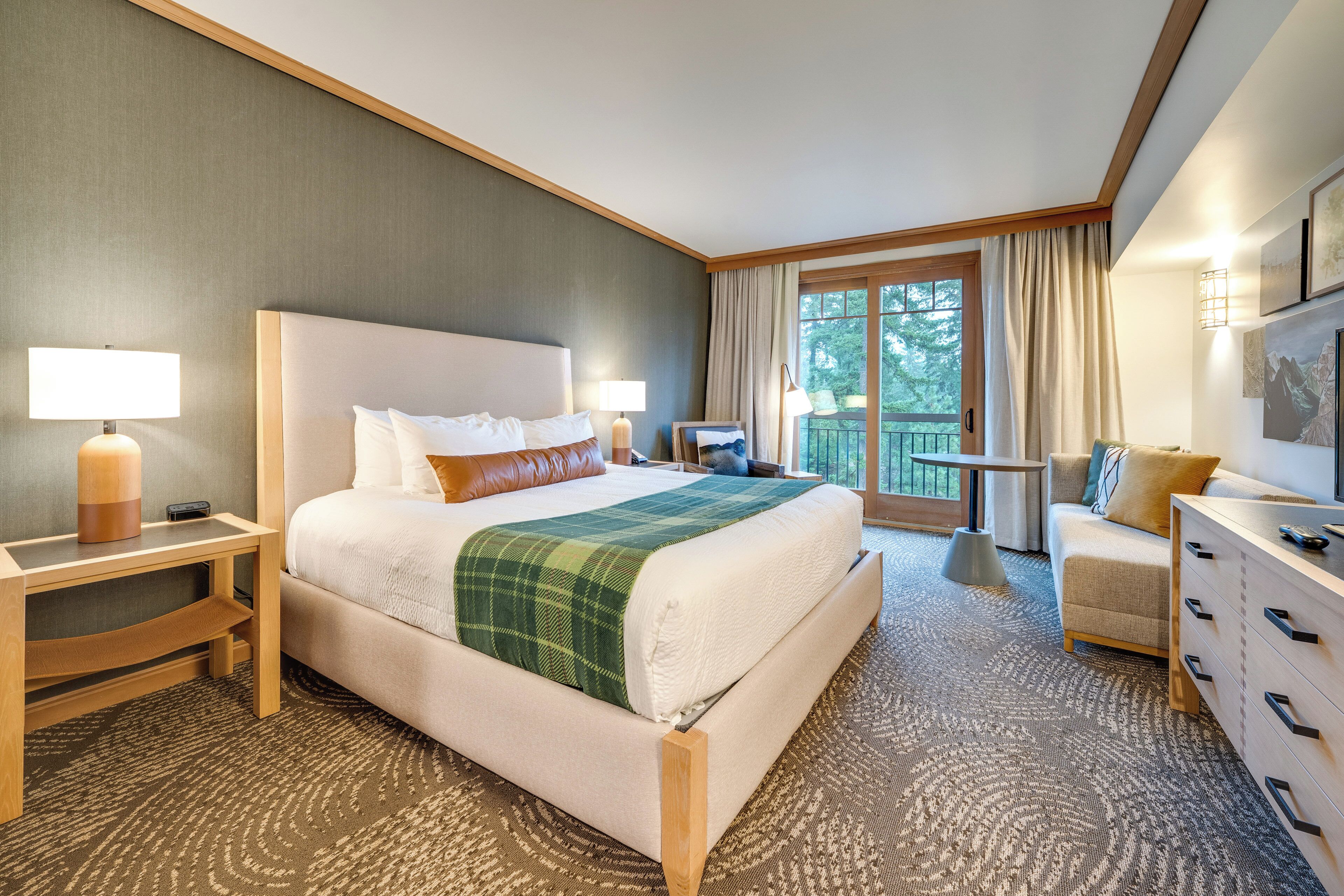 A hotel room with a large bed, a desk, a dresser, and a balcony with curtains.