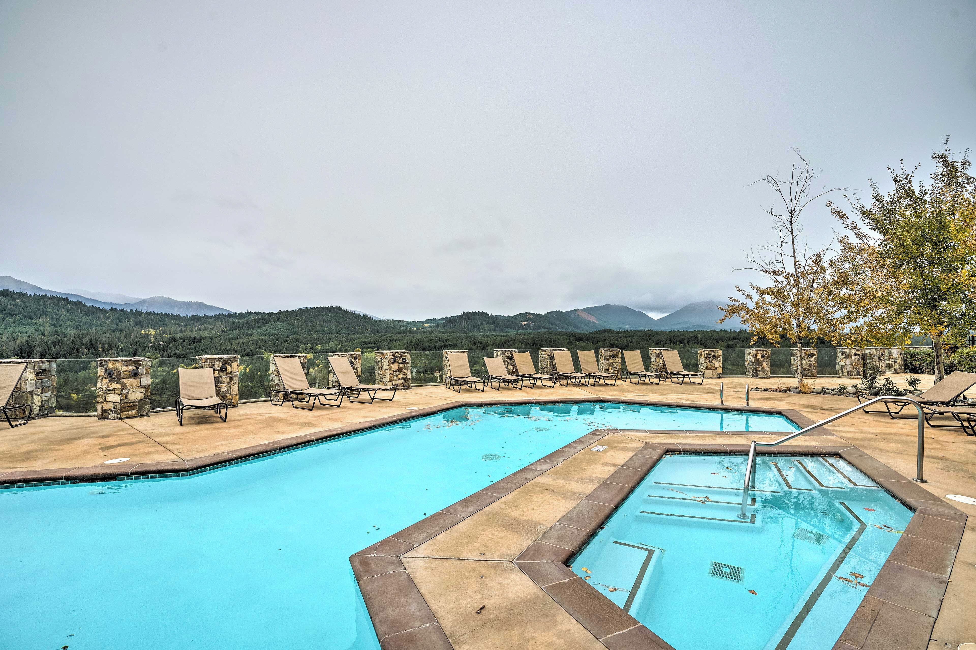 A swimming pool with lounge chairs and a stone wall, surrounded by mountains.