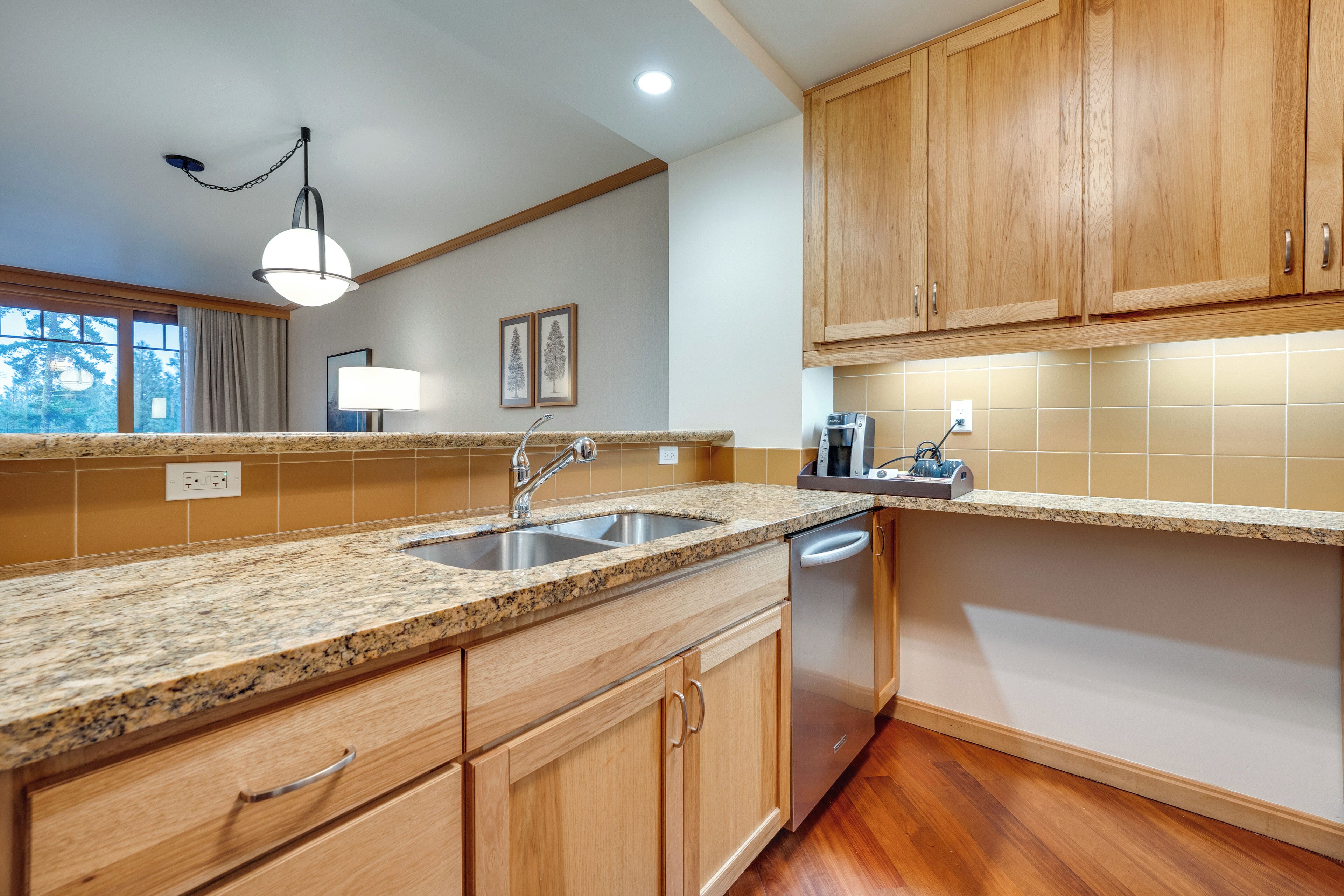 A kitchen with granite countertops, wooden cabinets, a dishwasher, and a window with curtains.