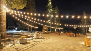 An outdoor patio area with string lights, seating, and a stone fireplace. - Valley-view Unit in Everline Resort: Premier Perks (Olympic Valley)