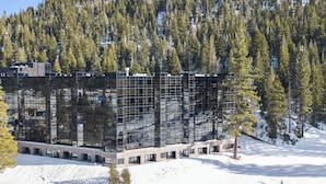 A modern building with a glass facade surrounded by a snowy landscape and dense forest. - Valley-view Unit in Everline Resort: Premier Perks (Olympic Valley)