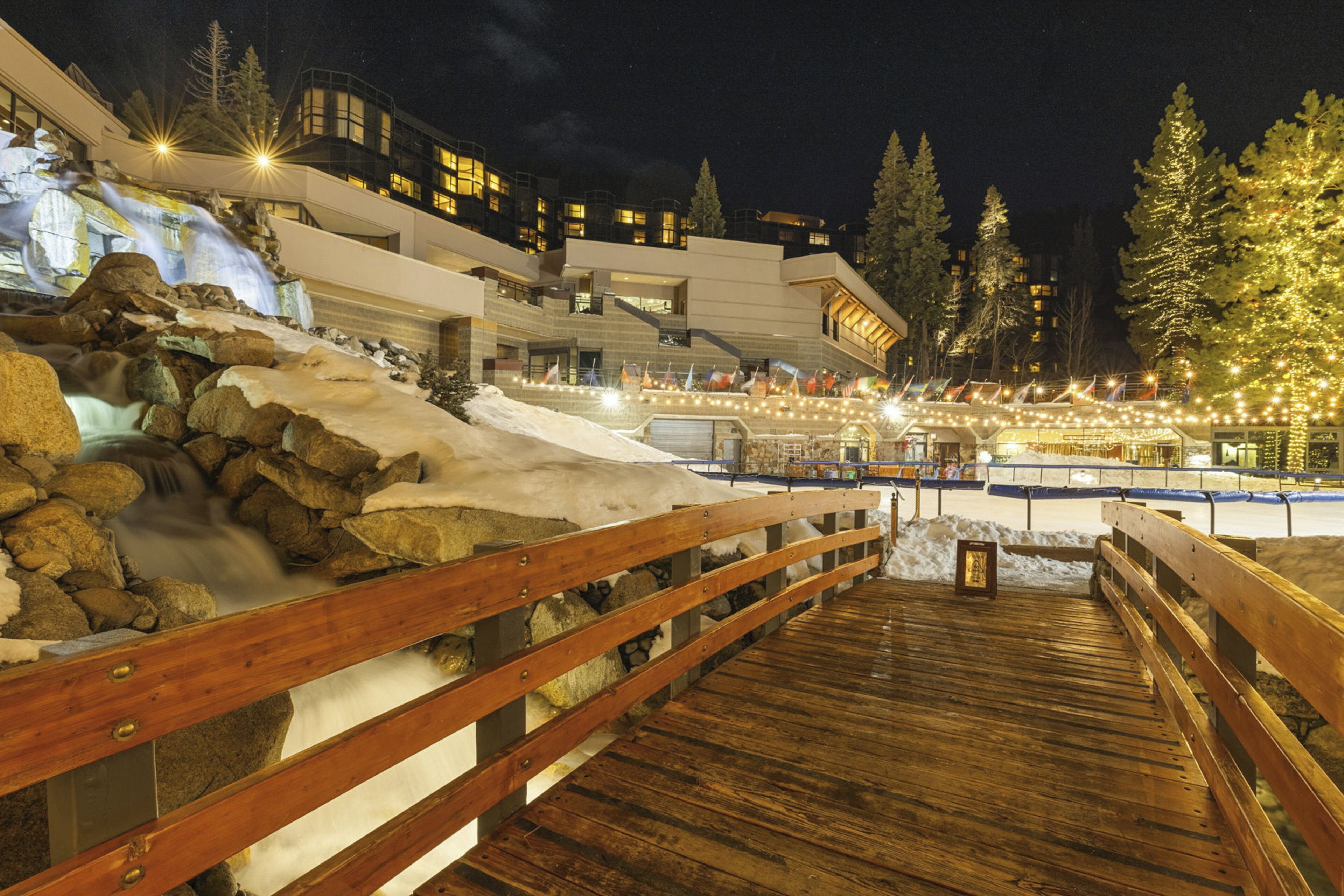 A wooden deck with a view of a building with multiple windows and a snow-covered landscape.