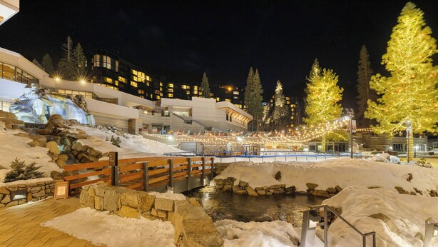 A snow-covered landscape with a wooden bridge, a stone wall, and a building with illuminated windows. - Pool, Hot Tub & Golf: Everline Resort Corner Suite (Olympic Valley)