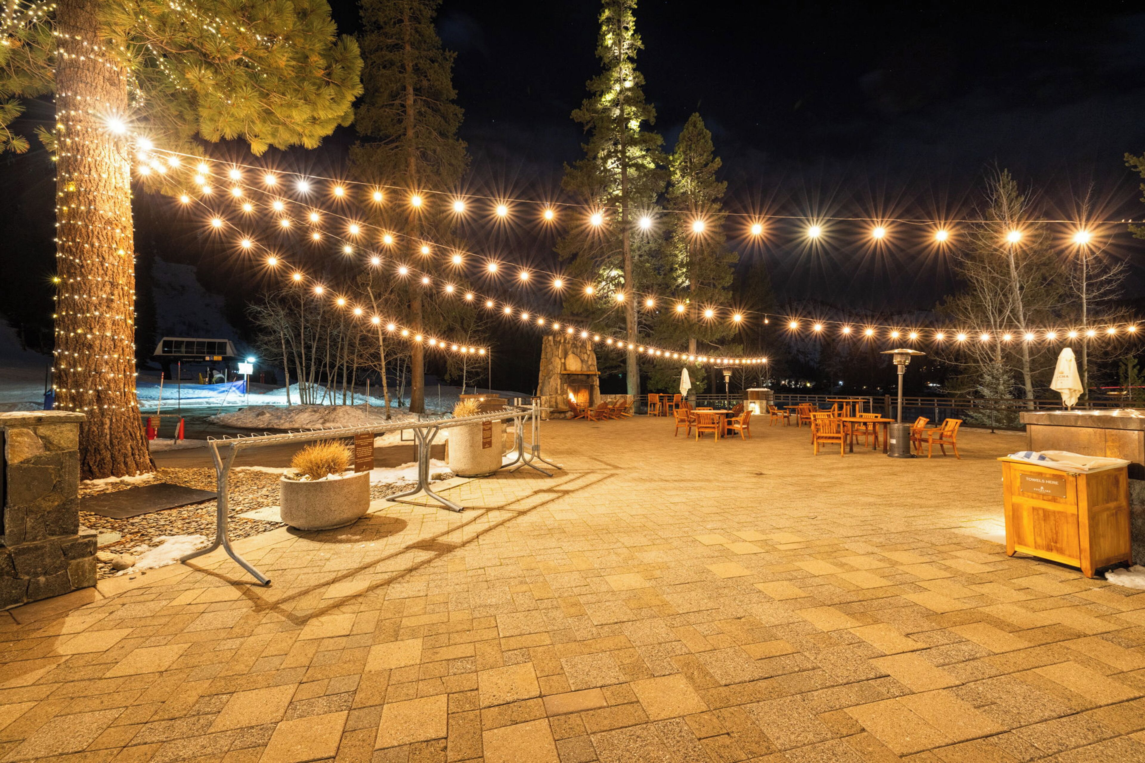 An outdoor patio area with string lights, seating, and a stone fireplace.
