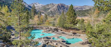 A resort with multiple swimming pools, a hot tub, and a mountainous backdrop.