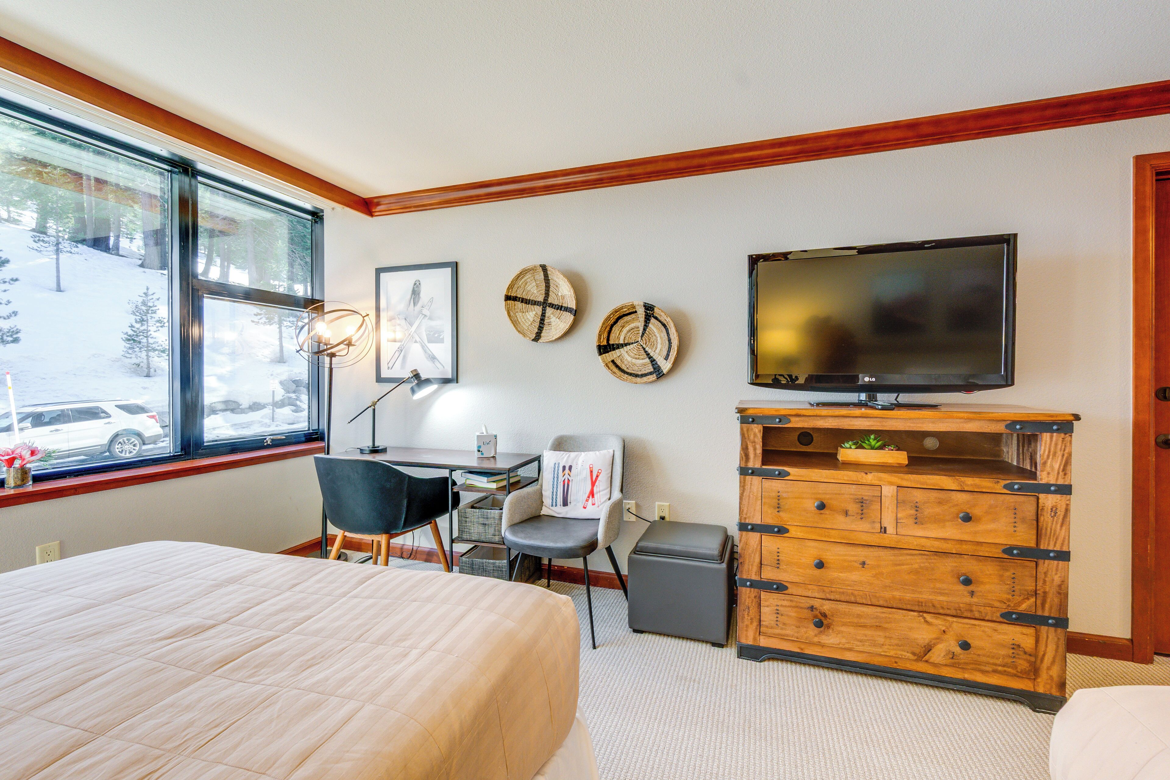 A hotel room with a bed, desk, chair, television, and a view of the outside.