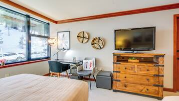 A hotel room with a bed, desk, chair, television, and a view of the outside.