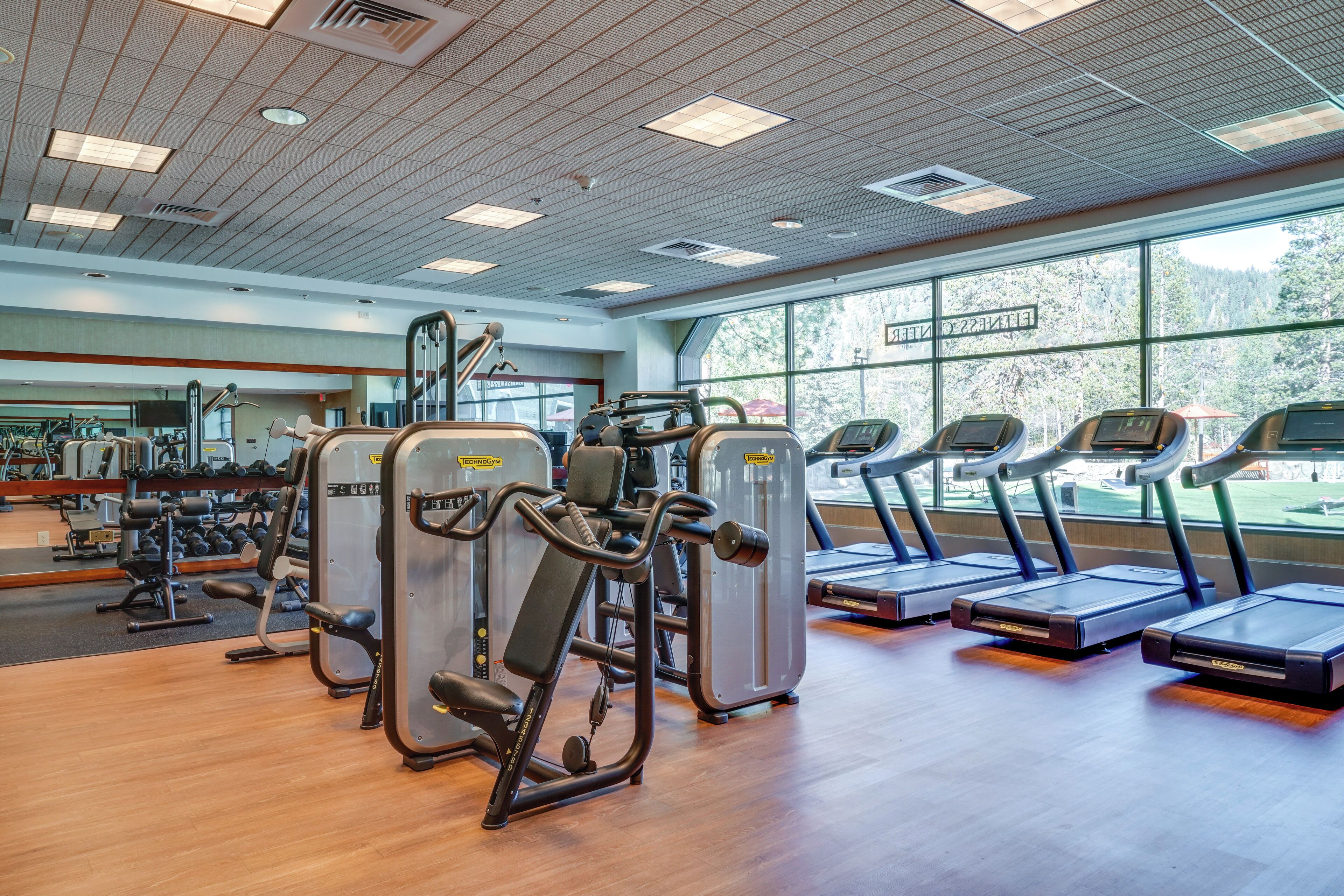 A gym with cardio machines, weight training equipment, and a large mirror.