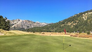 Een golfbaan met een vlaggenstok, bergen op de achtergrond en een heldere blauwe lucht.