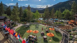 A resort with a pool, outdoor seating, and flags. - 1BR Condo w/ Access to Resort Pools, Spa & Gym (Olympic Valley)