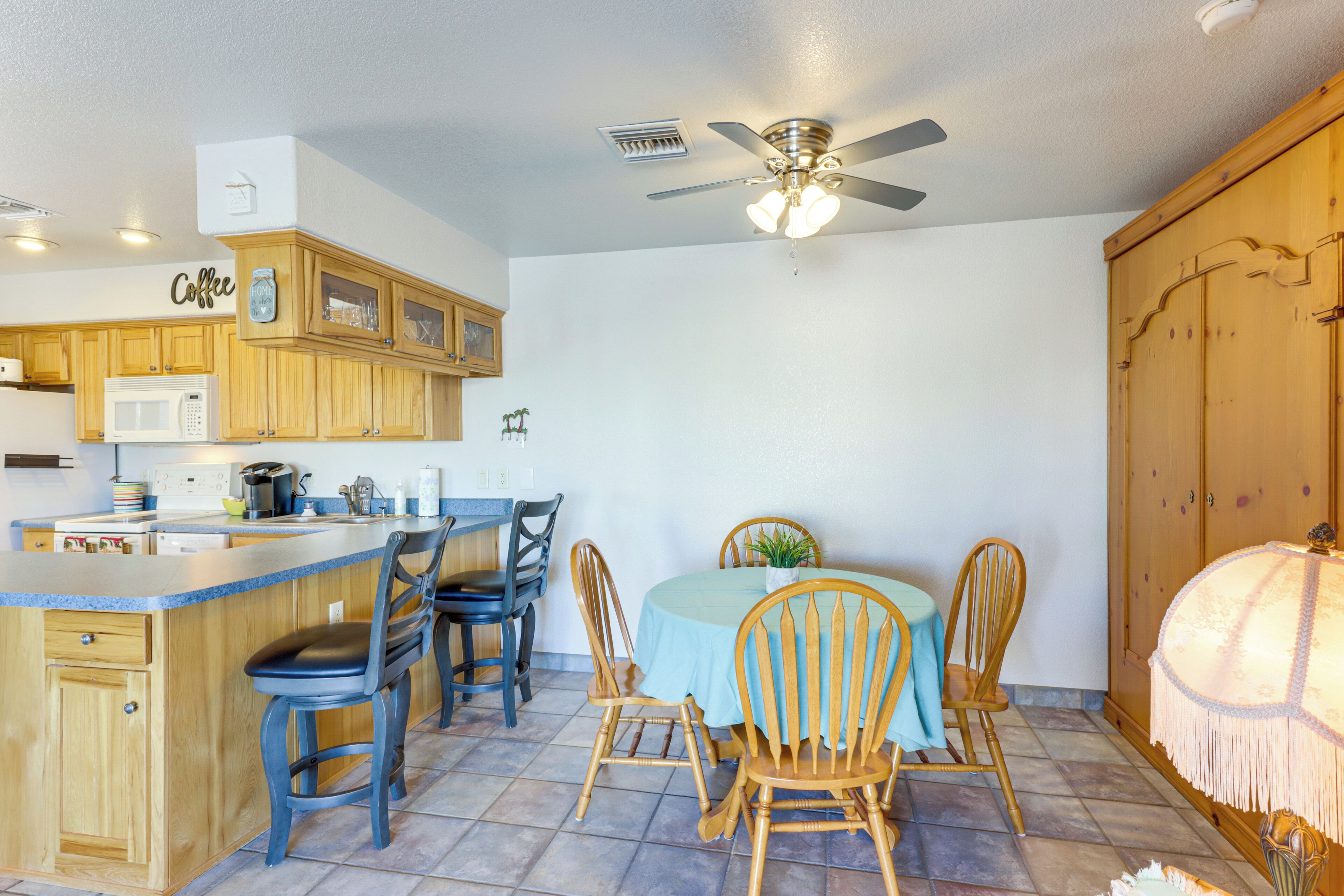A kitchen with wooden cabinets, a microwave, a coffee station, and a dining area with a table and chairs.