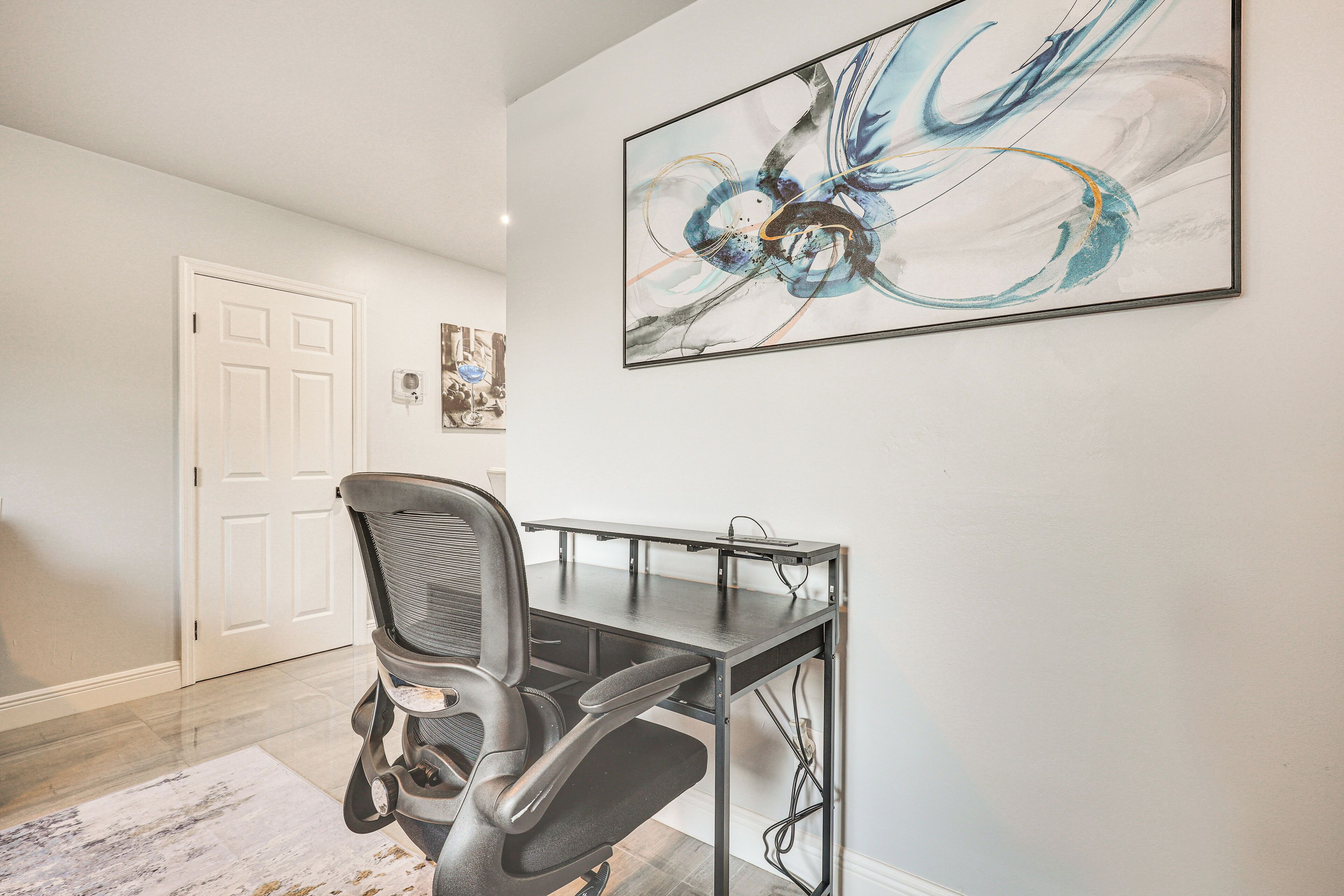 A modern office space with a desk and office chair, a large abstract painting on the wall, and a door in the background.
