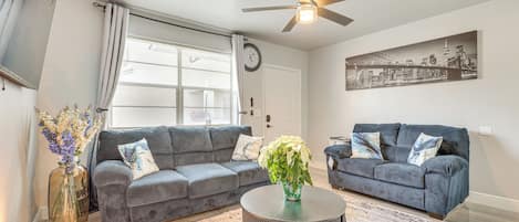 Un salon avec deux canapés, une table basse, une horloge et un ventilateur de plafond.