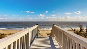 Ein hölzerner Steg führt zu einem Strand, im Hintergrund das Meer.