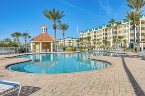 A swimming pool with lounge chairs, a small pavilion, and a hotel building with balconies and palm trees. - Resort Living! Ponce Inlet Condo Near Beach! (Ponce Inlet)