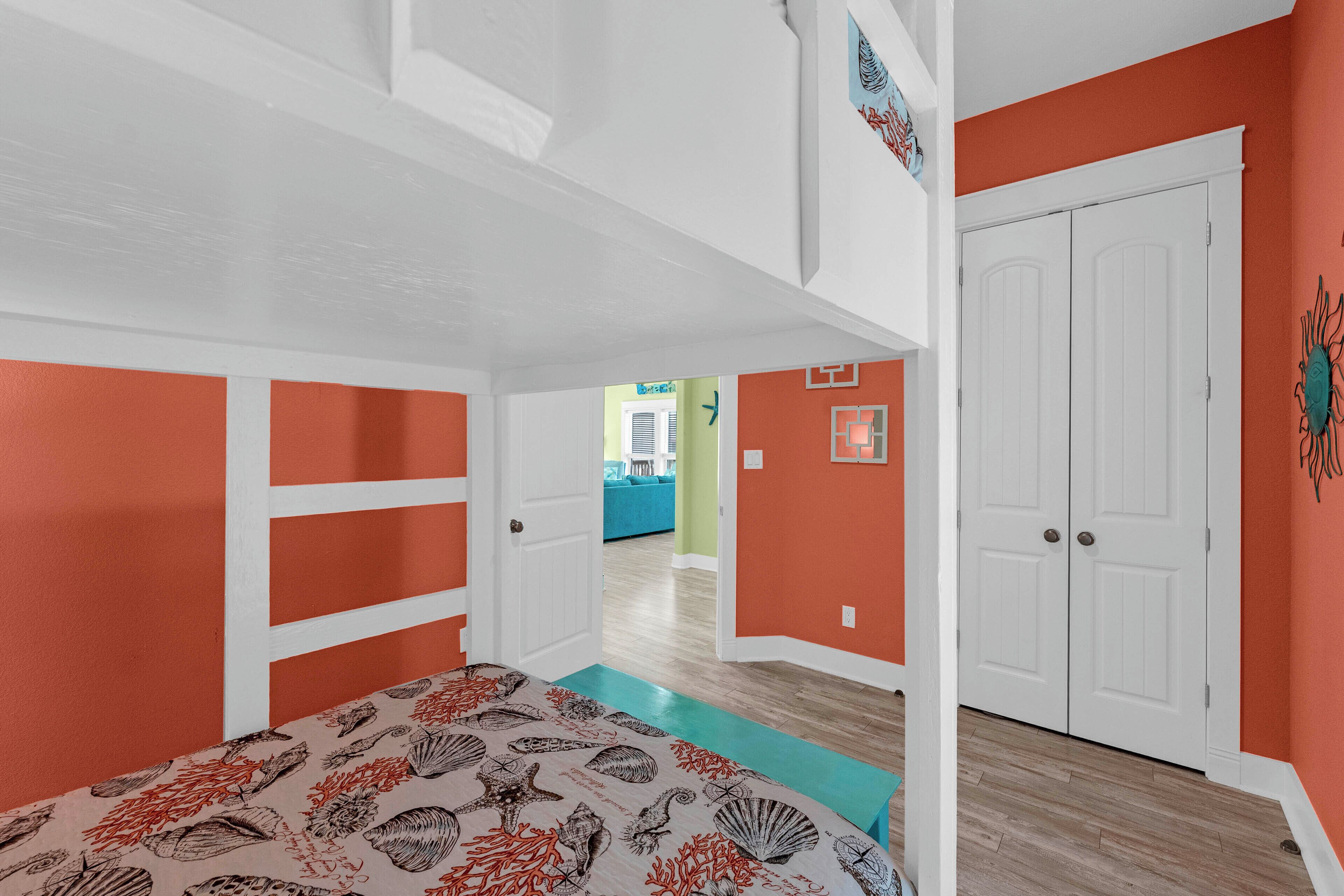 A bedroom with a bed, a white door, and a hallway leading to another room.