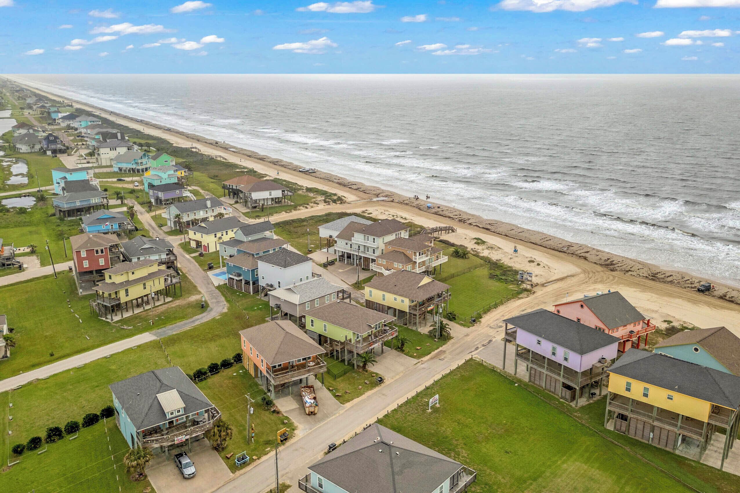 An aerial view of a coastal residential area with houses, a beach, and a road.