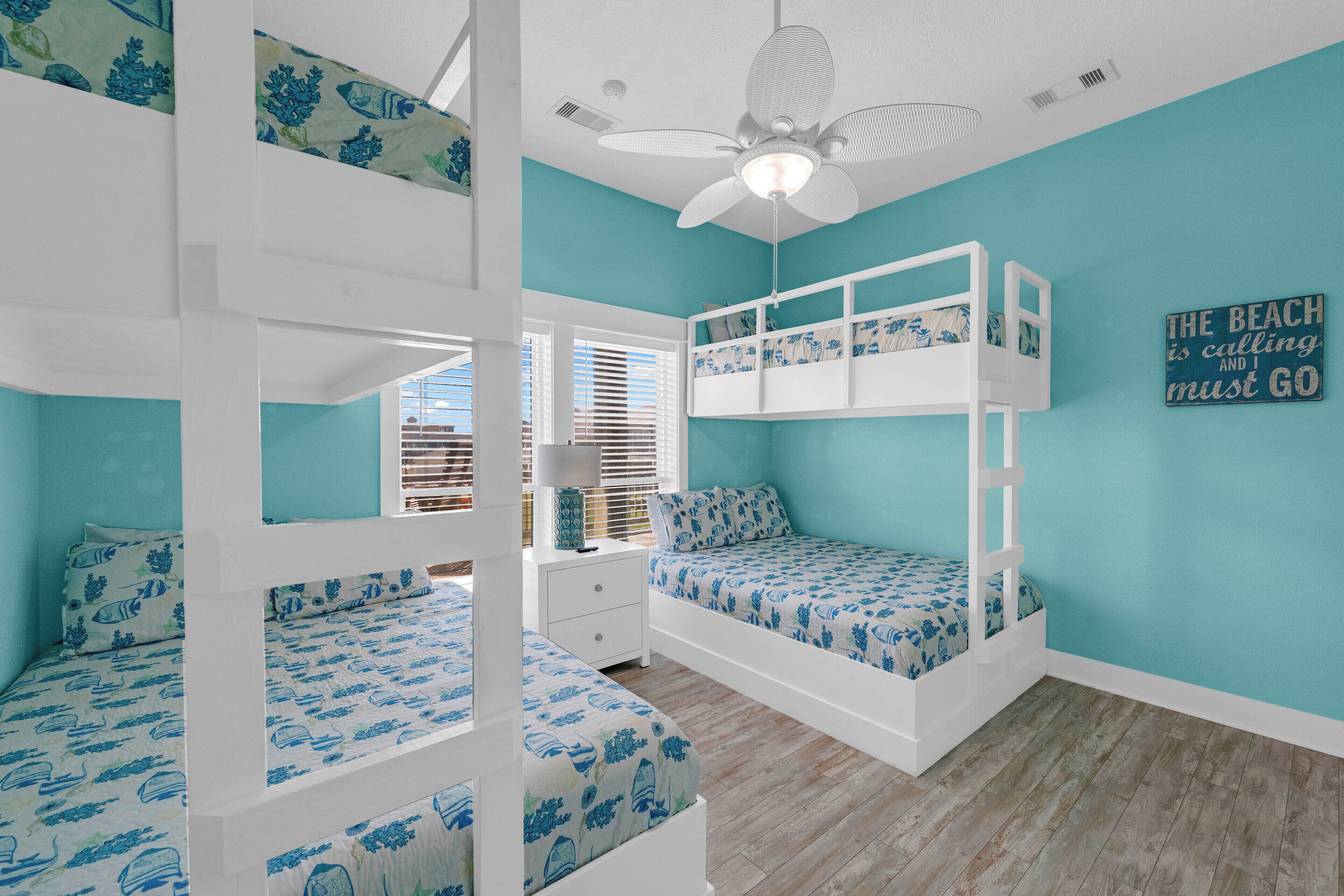 A room with bunk beds, a ceiling fan, a window with blinds, and a wall sign.