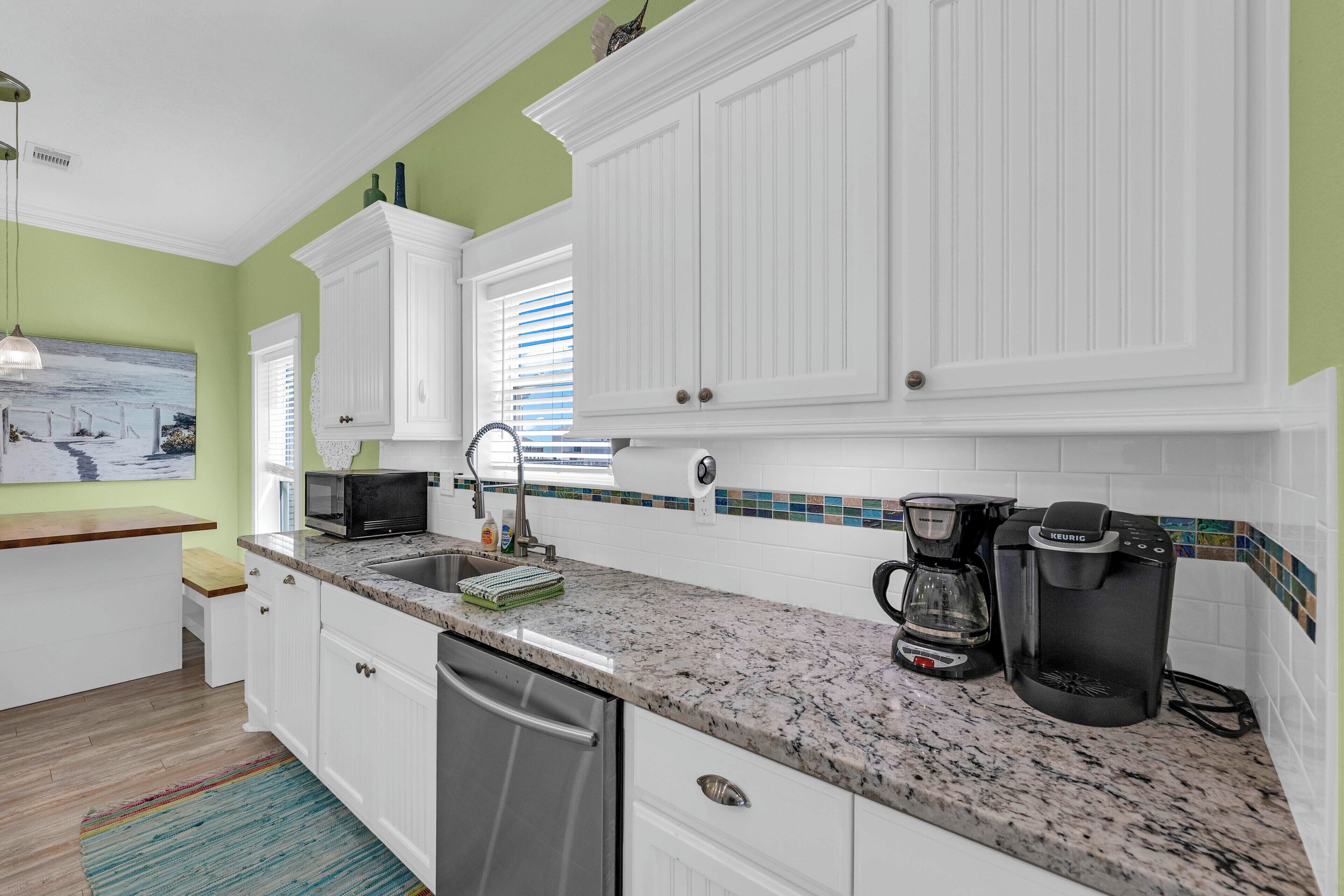 A kitchen with white cabinets, a granite countertop, a coffee maker, and a microwave.