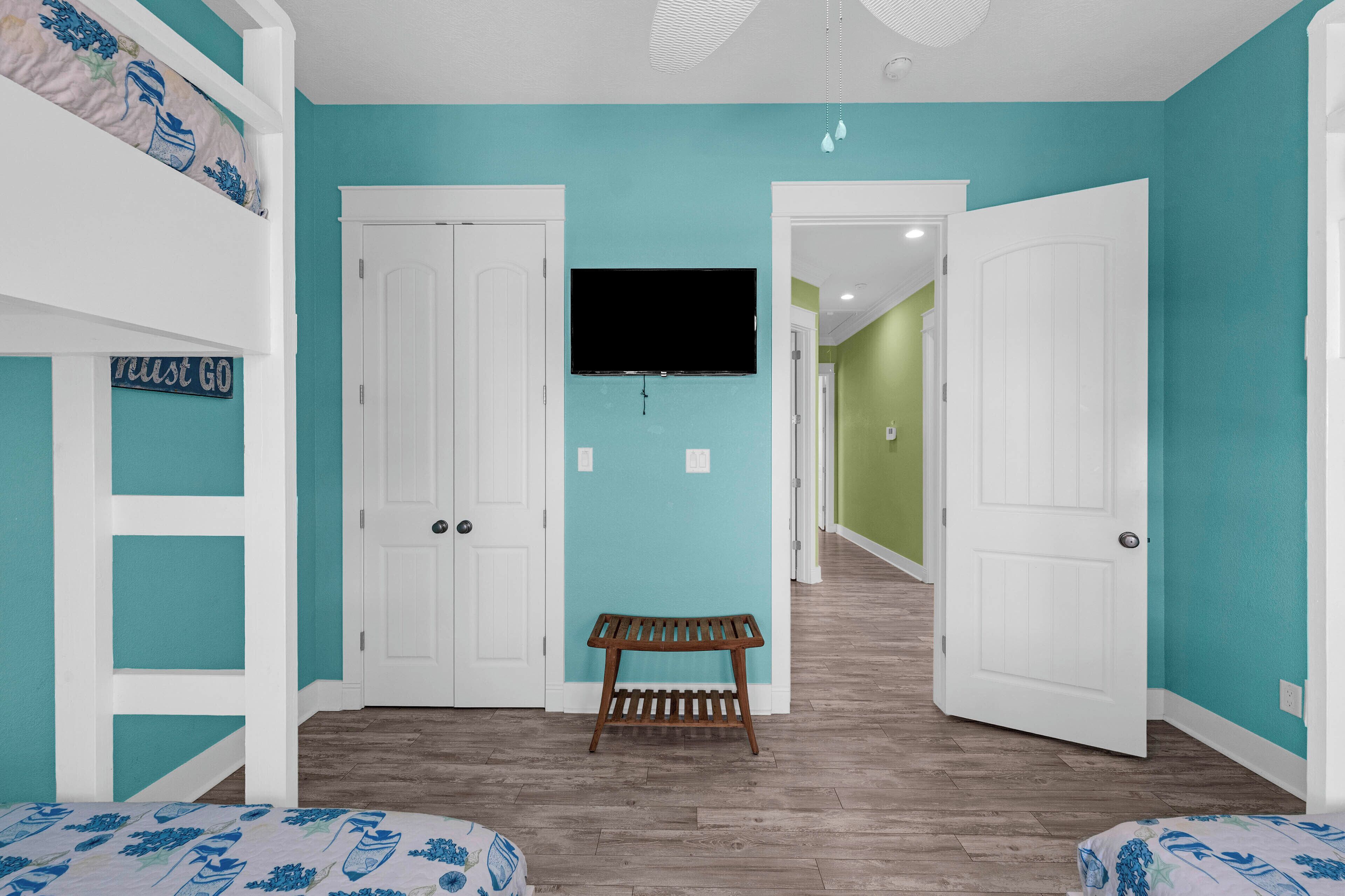 A room with teal walls, a bunk bed, a bench, and a TV on the wall.