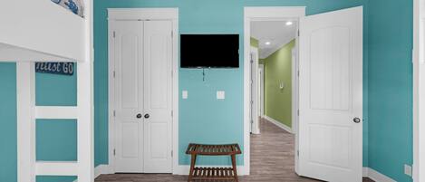 A room with teal walls, a bunk bed, a bench, and a TV on the wall.