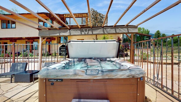A hot tub with a wooden exterior and a glass top, surrounded by a metal fence and a building with a stone facade in the background. - 4 BR Home w/ Pool, Hot Tub, Fireplaces, Grills (Arroyo Seco)