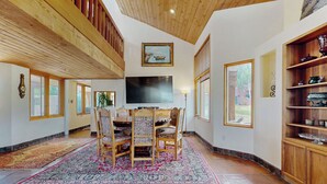 A spacious living room with a wooden ceiling, a large flat-screen TV, a dining table with chairs, and a decorative rug. - 4 BR Home w/ Pool, Hot Tub, Fireplaces, Grills (Arroyo Seco)