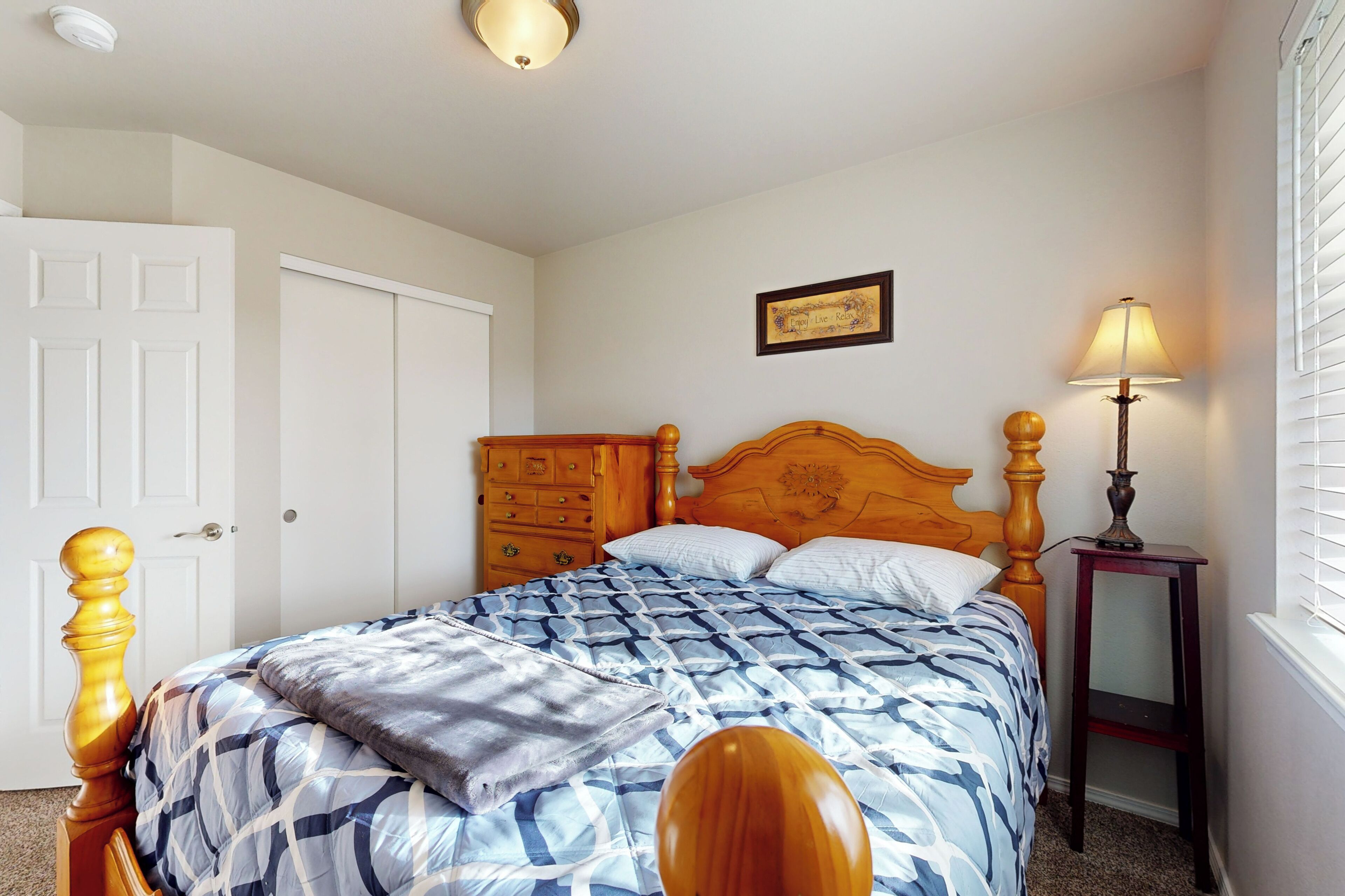 A bedroom with a wooden bed, a dresser, a nightstand with a lamp, and a framed picture on the wall.